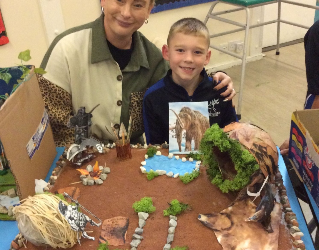 Picture showing pupil and parent sharing their fantastic model depicting a Stone Age scene.